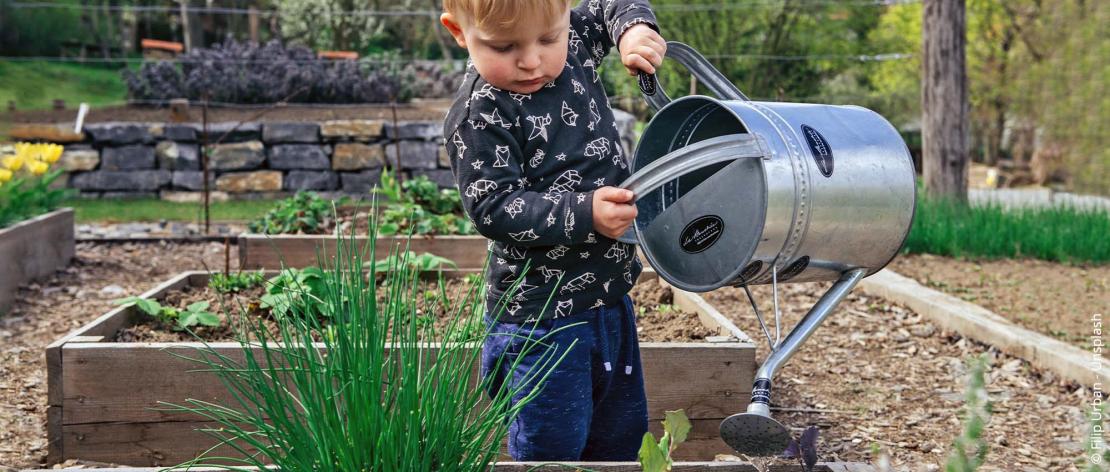 Kind geeft planten in verhoogde bedding water