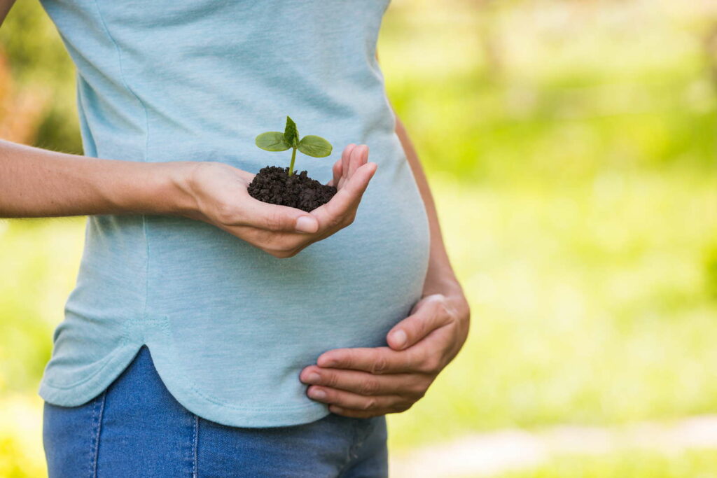 Zwangere vrouw met plant in de hand die buiten staat